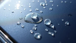 Close-up of water droplets beading on a glossy car paint surface with sunlight reflection, showing hydrophobic protection in action